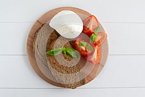 Large mozzarella with slices of tomatoes and basil on a wooden cutting board. Rustic style