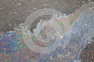 A large multi-colored spot from gasoline on the asphalt road quickly spreads over wet wet asphalt during rain, vertical photo