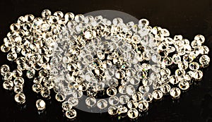 A large number of beautiful expensive diamonds with smooth edges on a black glossy background refract light rays