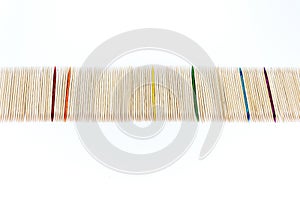 Large number of toothpicks lined up in a long row, with rainbow colored toothpicks interspersed, isolated on white