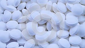 A large number of white pills lie together and rotate on a table close-up