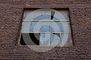 A large old broken window on a brown brick wall