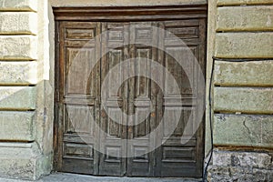 Large old brown wooden door on the concrete wall of the building