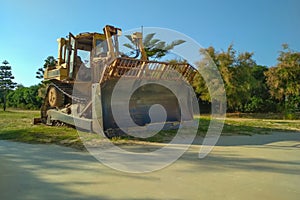 A large old bulldozer stands in a city park with a shovel lowered to the ground, defocused. Preparation for razing to