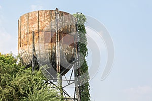 Large old iron water tank tower full of rust and covered trees  on blue sky background