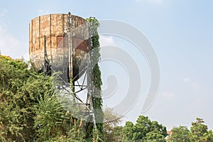Large old iron water tank tower full of rust and covered trees  on blue sky background