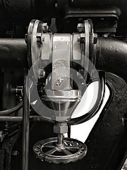 Large old metal industrial valve with round handle mounted on a large black machine with bolts and shiny pipes