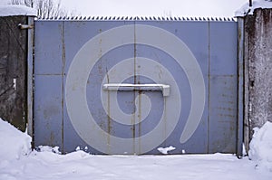 Large, old, rusty metal gates and a concrete fence block the way to the plant, on a cloudy winter day