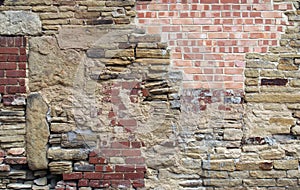 large old wall made of mixed bricks and stone with many jumbled patched and uneven repairs