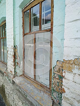 Large old window in a wooden frame. Brick house with shabby pale green paint.