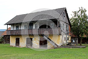 Large old wooden family house with raised front porch and dilapidated boards next to concrete well with rusted water pump