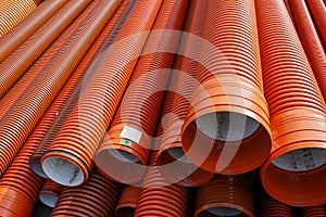 Stack of orange corrugated plastic pipes for construction and drainage infrastructure projects