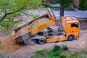A large orange dump truck unloads the sand.