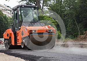 Large orange roller in the process of rolling hot asphalt
