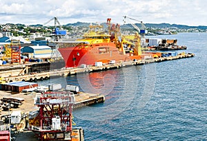 A large orange and yellow colored Offshore Construction Vessel OCV is in a dry dock of a shipyard and is being repaired