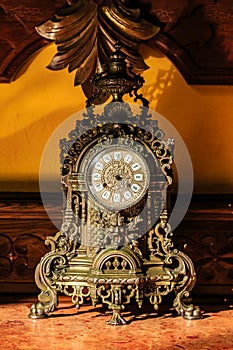 A large, ornate clock with a gold frame sits on a table photo