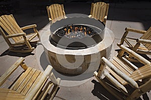 Large outdoor fire pit surrounded by wooden rocking chairs