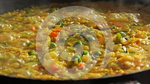 A large pan of bubbling risotto is boiling. Risotto with vegetables and pieces of chicken is prepared in the home