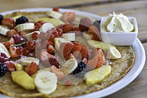 Large pancake with fresh summer fruit and whipped cream on a wooden table