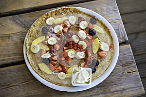 Large pancake with fresh summer fruit and whipped cream on a wooden table. Top view