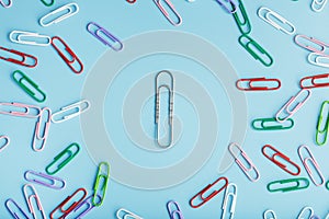 A large paper clip surrounded by small colored paper clips on a blue background