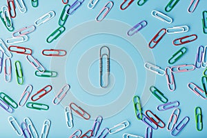 A large paper clip surrounded by small colored paper clips on a blue background