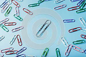 A large paper clip surrounded by small colored paper clips on a blue background