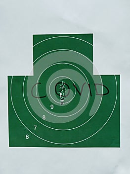 A large paper green target that says COVID. The holes in the center of the target