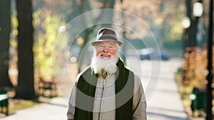 In the large park in the autumn good looking old man posing in front of the camera smiling large and feeling excited