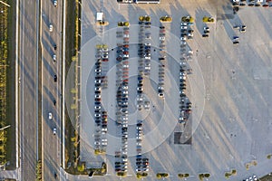 Large parking lot of local dealer with many brand new cars parked for sale on highway roadside. Development of american