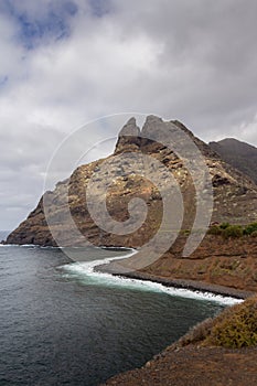 large pebble mountain by the calm sea in an arid environment of the canary islands under cloudy skies