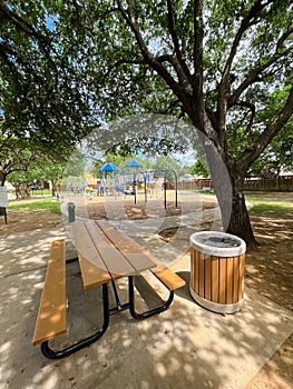 Large picnic table with trash can under mature oak tree shade, drinking water fountain near playground climbing structure