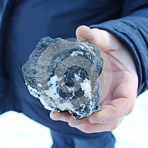 A large piece of coal under the snow in a man`s hand.