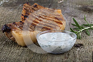 Large piece of fresh pork meat on a bone prepared on a grill pan with souse on old wooden table for background