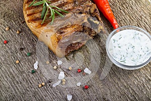 Large piece of fresh pork meat on a bone prepared on a grill pan with souse and vegetables on old wooden table for background