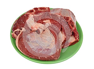 A large piece of raw beef with bones and ribs on a green plate isolated
