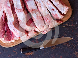 A large piece of raw pork meat chopped into pieces on a cutting board on an old rustic table black and stainless steel kitchen