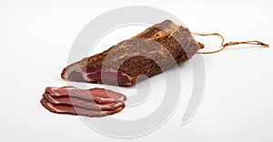 Large piece of uncooked smoked pork delicacy in a spice sprinkle with slices on a white background