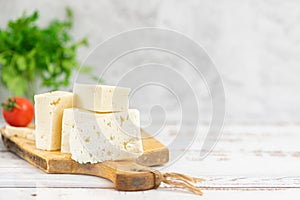 Large pieces of feta cheese on old wooden cutting board and cherry tomatoes on light background. Selective focus