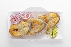 Large pieces of fried fish - pike perch with red onion and lime in a white plate on a light background.