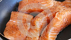 Large pieces of red salmon fish fillets are fried in a pan