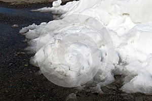 A large pile of dirty white snow lies on the asphalt road