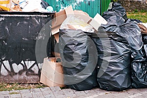 Large pile of household rubbish in black plastic bags near a dumpster in a big city