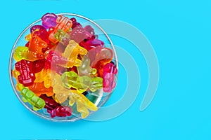 A large pile of multi-colored jelly marmalade candies in a glass bowl on a blue background