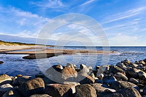 A large pile of stones lies near the seashore. An old stone breakwater or pier at low tide