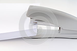 Large pile of white paper is placed in a small office stapler, concept abstract background