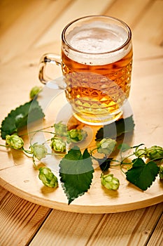 Large pint of beer with foam and sprigs of hops on wooden table