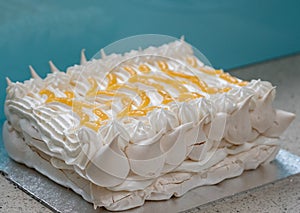 Large piped meringue pavlova cake, decorated with piped cream and lemon curd in a herringbone pattern.
