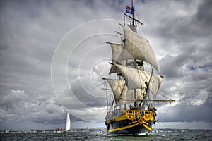 Large pirate sailboat in the open ocean under a cloudy sky