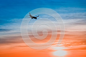 Large plane flies in the evening sunset sky, dramatic painted sky and airplane silhouette with clouds over Lisbon in Portugal